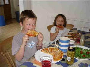 Two children sitting at home eating pizza